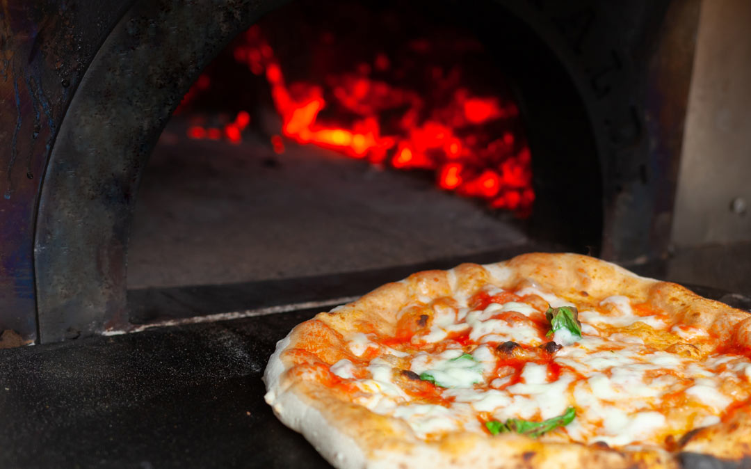 a margherita pizza sliding out of a pizza oven