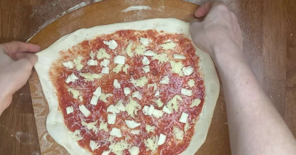 homemade pizza dough with toppings being dragged onto a pizza peel covered in semolina flour