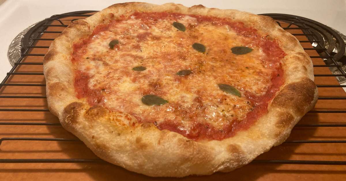 a well-done homemade pizza sitting on a pizza peel with a puffy browned crust