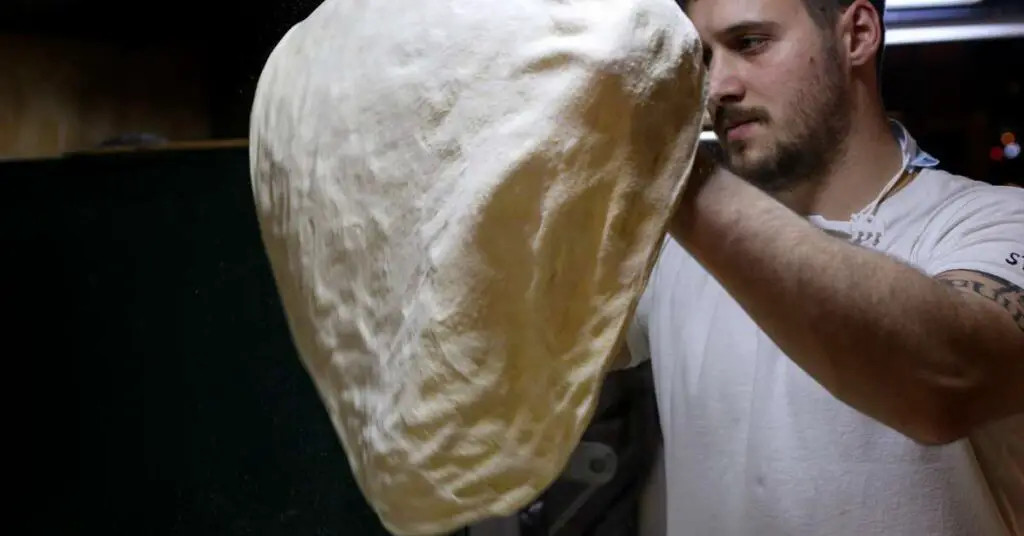 A pizza chef stretching pizza dough by hand.