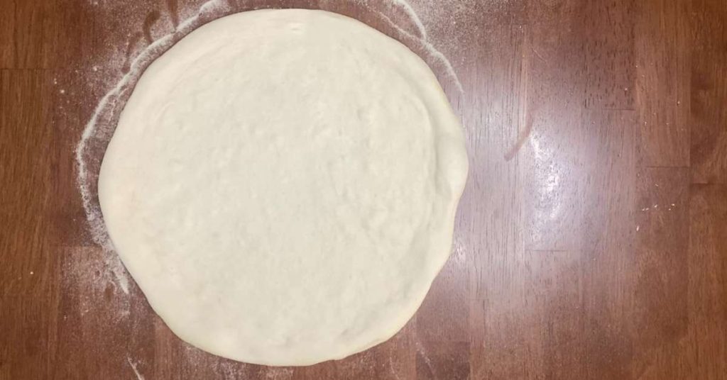 homemade pizza dough on a brown table waiting to be topped