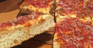 A slice of Detroit style pizza with a thick crust and melted cheese.