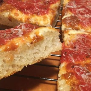 A slice of Detroit style pizza with a thick crust and melted cheese.