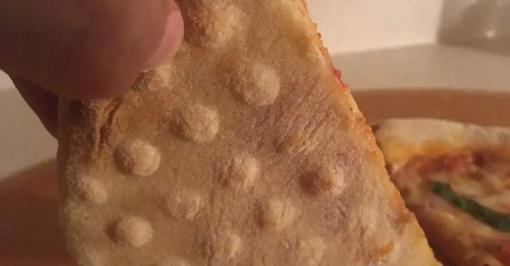 A slice of pizza cooked on a perforated pizza pan with holes in it.