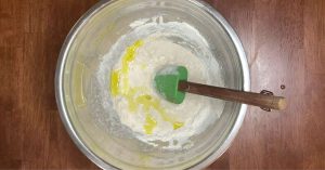 adding olive oil to a pizza dough recipe in a mixing bowl