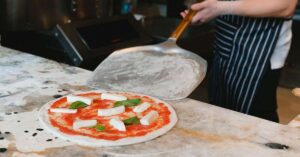 A chef using a pizza peel to carry a pizza over to a pizza oven.