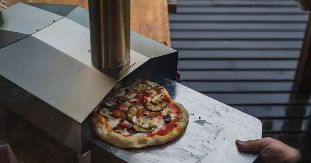 Using a pizza peel to pull a pizza out from a portable pizza oven.