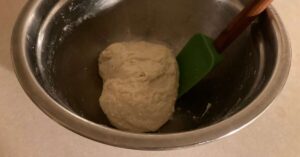 A roughly mixed ball of pizza dough in a metal bowl.