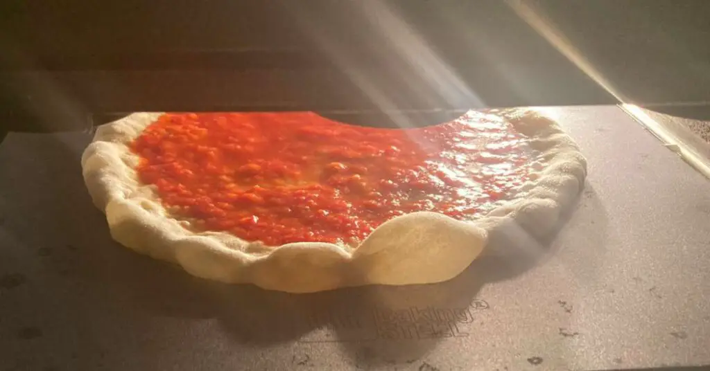 A marinara pizza cooking on a large 14 x 16 inch pizza steel in a home oven.