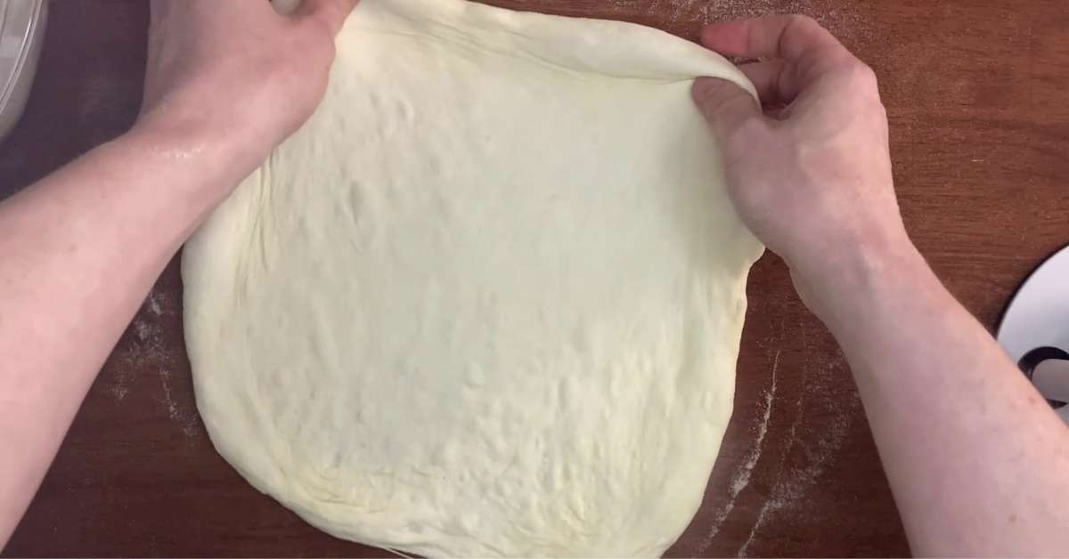 Two hands stretching pizza dough.