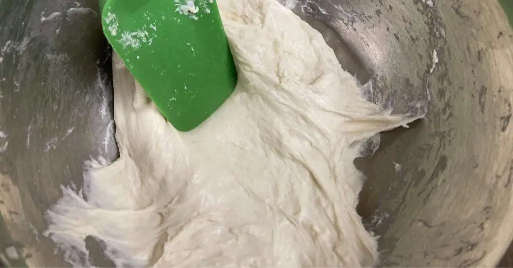 A green spatula poking pizza dough in a mixing bowl.