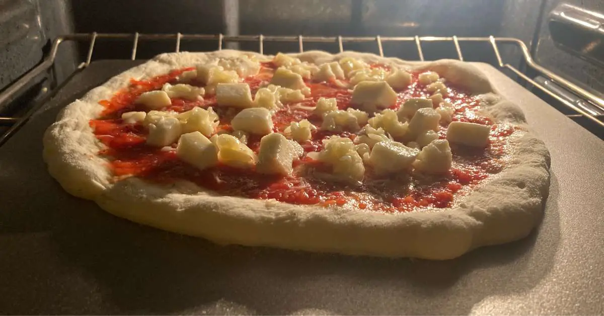 A homemade margherita pizza cooking on a pizza steel in a home oven.