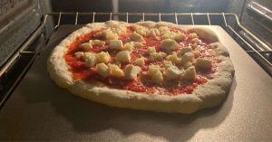A pizza with tomato sauce and cheese cooking on a pizza steel in a home oven.