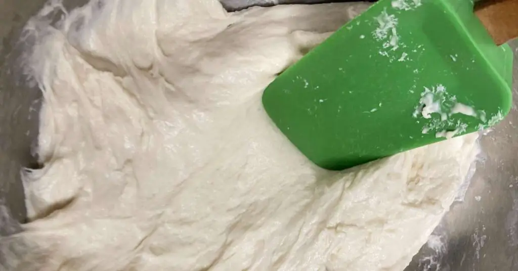 mixing pizza dough in a mixing bowl with a green spatula