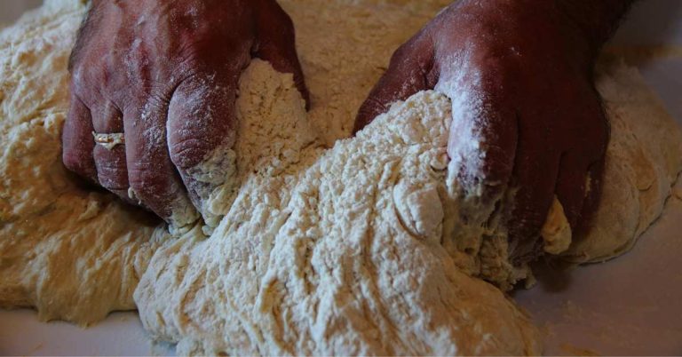 A close up shot of a man's hands kneading pizza dough, serving as the icon for the debate between all-purpose flour vs 00 flour for making pizza.