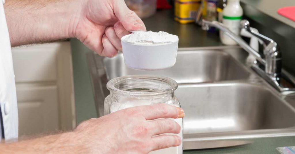 A man scooping flour from a jar to make pizza.