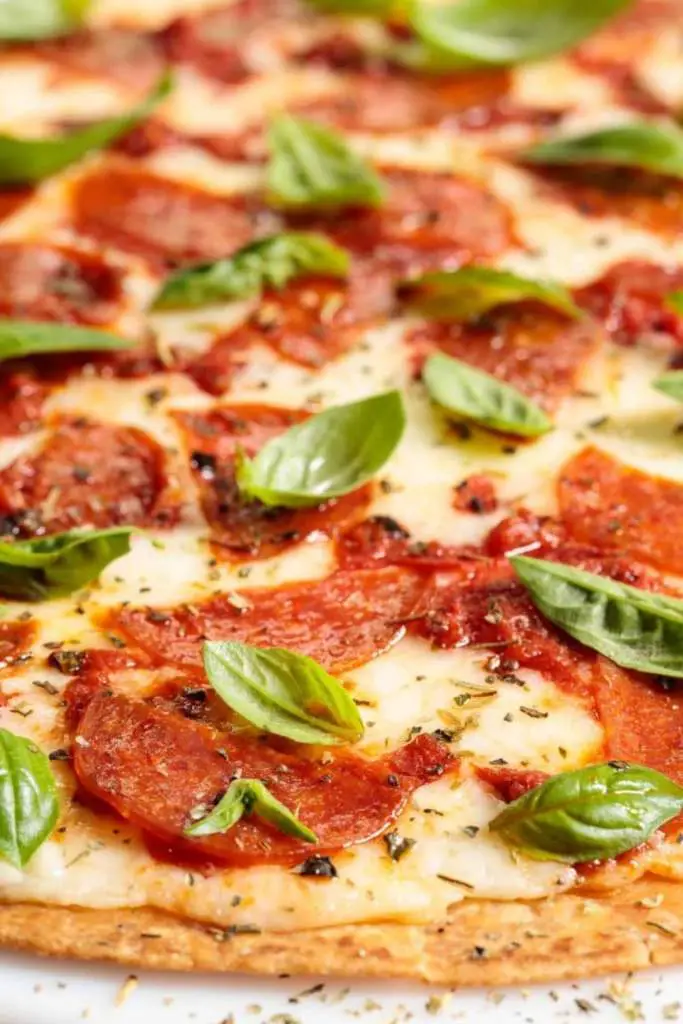 10 Delicious Thin Crust Pizza Recipes You Have To Try 3 A close-up of a crispy pepperoni pizza, topped with fresh basil leaves.