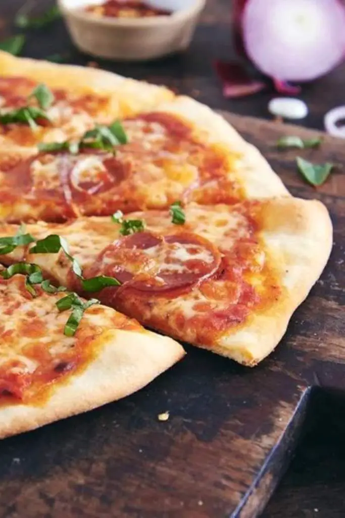 10 Delicious Thin Crust Pizza Recipes You Have To Try 7 A homemade pizza with a thin, chewy crust, topped with sauce, cheese, and pepperoni, on a wooden board.