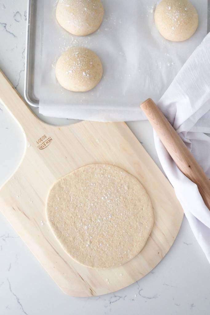 10 Delicious Thin Crust Pizza Recipes You Have To Try 10 A thin pizza dough rolled out on a pizza peel, with proofed dough balls in the background.