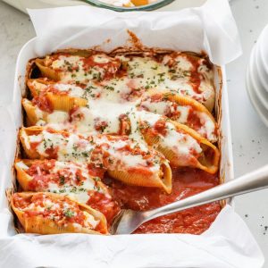Photo taken from a top-down angle, using all-natural lighting, showing the stuffed shells in a baking dish, topped with marinara sauce and shredded mozzarella, ready for baking, on a light gray concrete countertop.