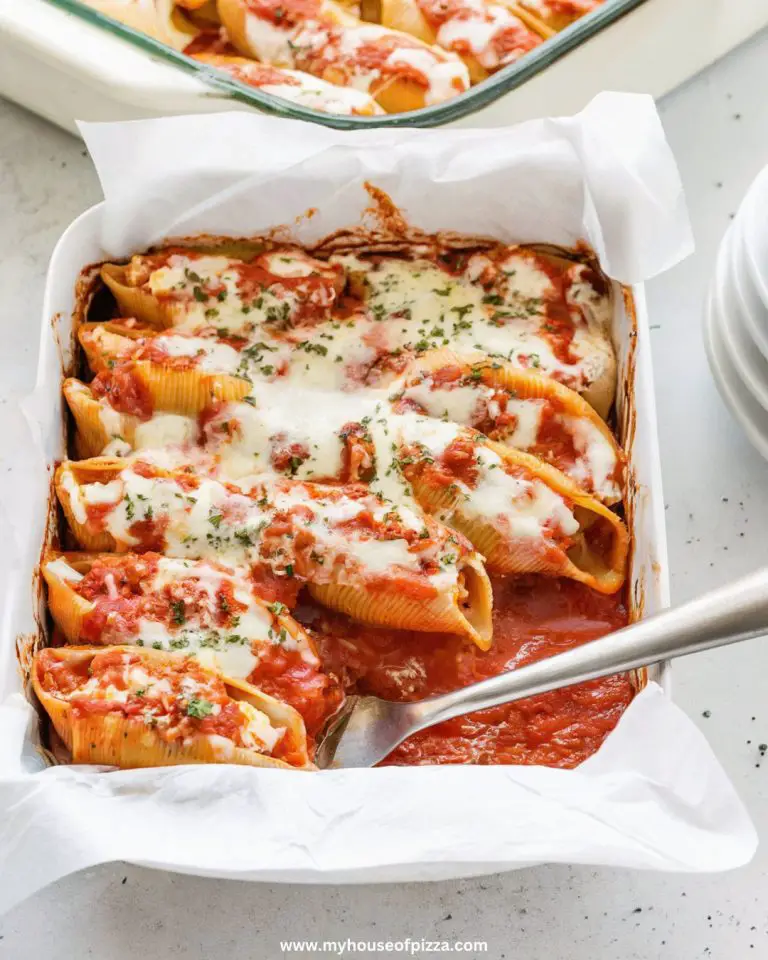 Photo taken from a top-down angle, using all-natural lighting, showing the stuffed shells in a baking dish, topped with marinara sauce and shredded mozzarella, ready for baking, on a light gray concrete countertop.