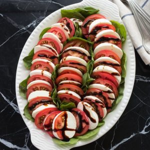 Fresh and Easy Caprese Salad Recipe for a Healthy Italian Delight 7 A beautifully arranged Caprese salad on a white platter features alternating slices of ripe tomatoes and fresh mozzarella, garnished with basil leaves and drizzled with balsamic glaze.