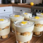 Delicious lemon dessert served in clear glasses, featuring layers of creamy lemon mousse and soft ladyfinger cookies, topped with bright yellow lemon zest for an eye-catching presentation. Perfect for serving at parties or as a refreshing treat.