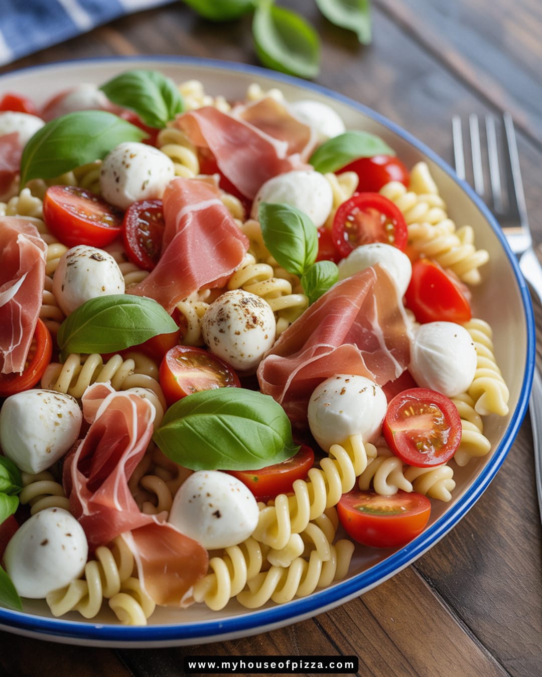 Summer Italian Pasta Salad with Mozzarella and Prosciutto Recipe 1 A beautifully arranged Classic Italian Pasta Salad featuring tri-color rotini pasta, fresh mozzarella balls, cherry tomatoes, and thinly sliced prosciutto, garnished with vibrant basil leaves, perfect for summer picnics or gatherings.