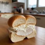 A delicious ice cream sandwich featuring creamy filling nestled between two soft, buttery buns, set against a kitchen backdrop, perfect for a sweet treat or dessert recipe.
